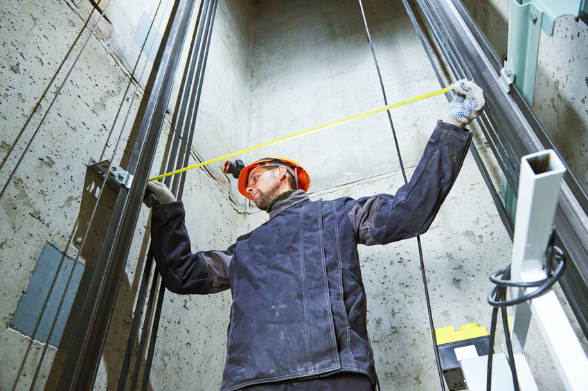 machinist with measure tape checking lift construction in elevator
